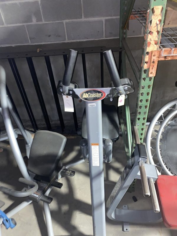 A rowing machine alongside other new and remanufactured gym equipment in a garage, including the Abs Coasters Elite - As Is Functional.