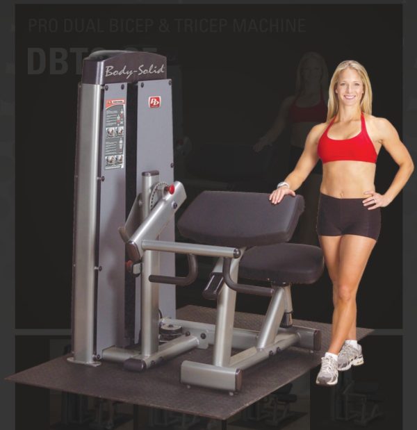 A woman is posing next to a new Body Solid DBTC-SF Pro Dual Bicep/Tricep Machine.