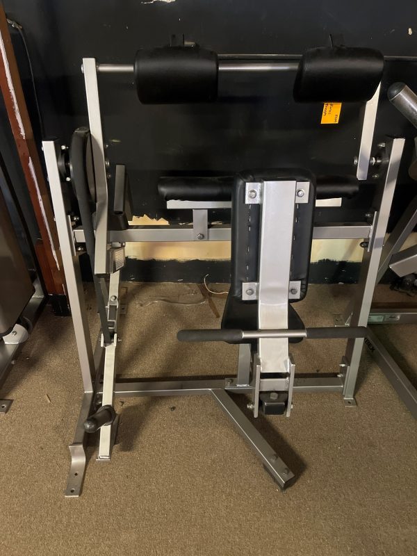 The remanufactured Hammer Strength Plate Loaded Tricep features padded supports and a sturdy metal frame, set against a dark wall on the carpeted floor.