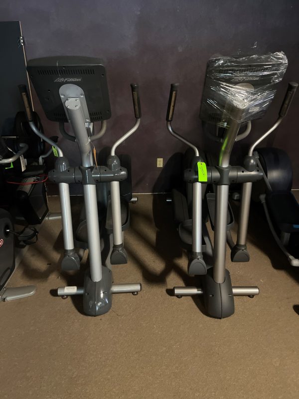 Two Life Fitness CLSX Ellipticals - Remanufactured, stand side by side in the gym, exuding a high-end vibe. One machine's console is protected with plastic wrapping, ready for action.