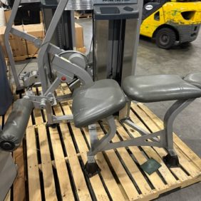 A Nautilus Nitro Prone Leg Curl - As Is Functional machine is placed on a wooden pallet within an operational warehouse environment. In the background, a yellow forklift stands ready to provide efficient transport.