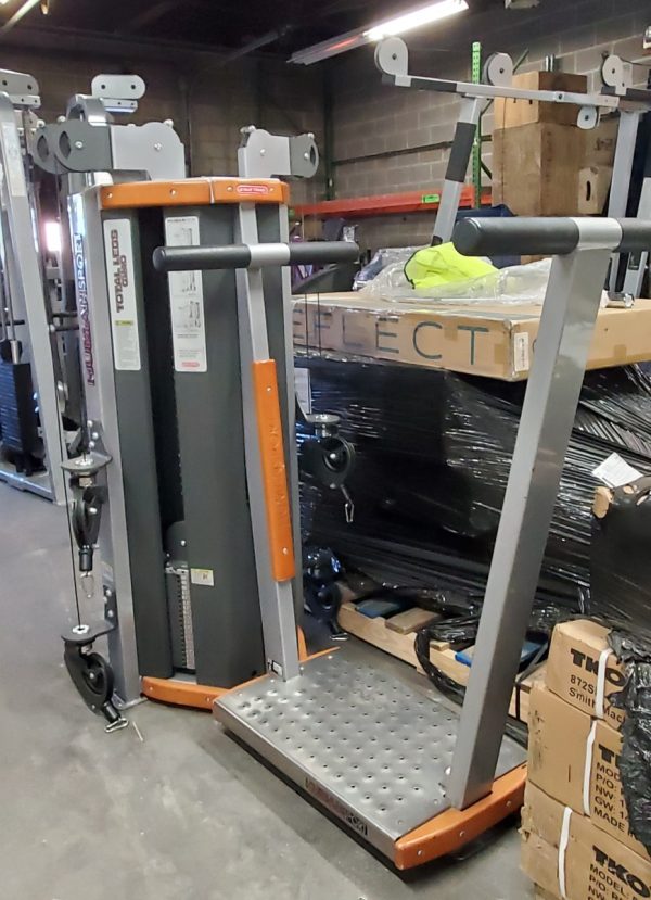 A Star Trac Human Sport Total Leg - As Is Functional machine sits amidst boxes and equipment in a storage area, blending seamlessly into the dynamic environment.