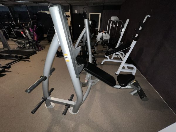 In a dim gym among the equipment, a remanufactured weight bench with padded seat and backrest stands next to the versatile Precor Stretch Machine - Remanufactured, inviting fitness enthusiasts to enjoy a comprehensive workout experience.