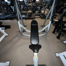 A gym bench is centered in a fitness facility filled with various exercise equipment, including a remanufactured Precor Stretch Machine - Remanufactured.