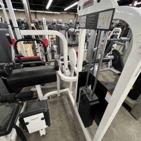 A remanufactured leg press machine with weights, outfitted in white and black, is surrounded by other exercise equipment in the gym, including a Precor Stretch Machine - Remanufactured.