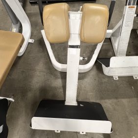 A remanufactured Precor Stretch Machine with light brown padding sits elegantly on the concrete floor, showcasing its sleek design.