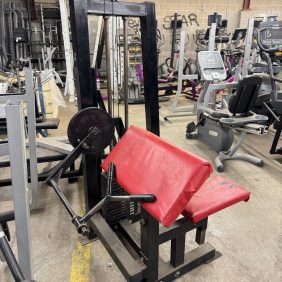 A cluttered room with gym gear, including a Life Fitness Signature Ab Crunch machine in black for $1995, stands amongst various exercise machines and graffiti-covered walls.