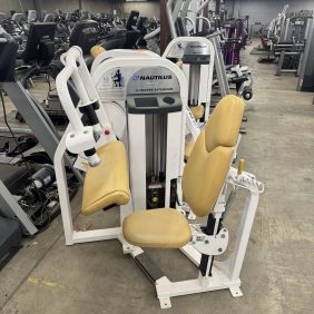 The Nautilus Nitro Plus Seated Calf machine, featuring beige cushioning, stands out in the gym with its sleek design. Surrounded by other functional fitness equipment, it enhances a comprehensive workout experience.