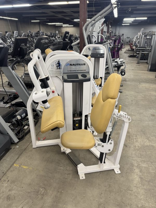 The Nautilus Nitro Plus Seated Calf machine, featuring beige cushioning, stands out in the gym with its sleek design. Surrounded by other functional fitness equipment, it enhances a comprehensive workout experience.