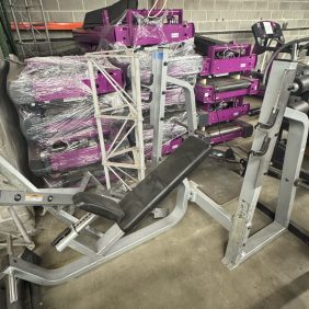 Gym equipment and machines stacked in a storage area with a concrete wall background.