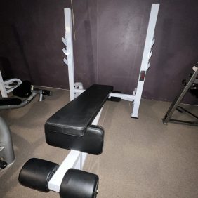 Positioned against a dark wall on a carpeted floor, the remanufactured weight bench with padded backrest and leg support reflects the functionality of the Precor Stretch Machine.