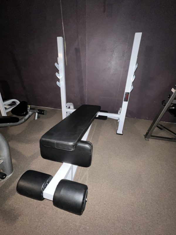 Positioned against a dark wall on a carpeted floor, the remanufactured weight bench with padded backrest and leg support reflects the functionality of the Precor Stretch Machine.