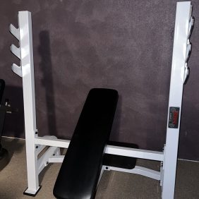 A remanufactured Precor Stretch Machine in white, featuring a black seat, is positioned against a dark wall and carpeted floor, seamlessly blending function and style.