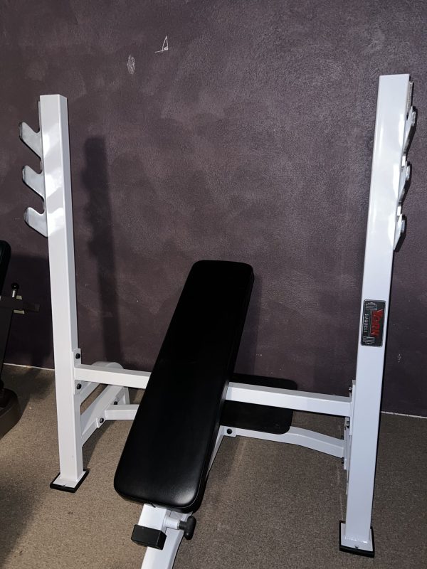 A remanufactured Precor Stretch Machine in white, featuring a black seat, is positioned against a dark wall and carpeted floor, seamlessly blending function and style.